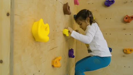 Medium-shot-of-a-little-girl-climbing-a-rock-climbing-wall