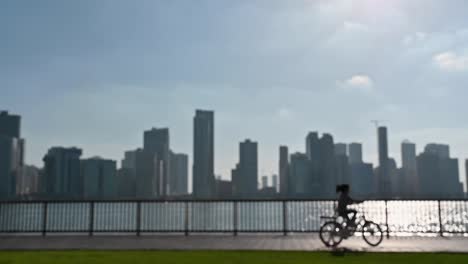 Slow-motion,-Out-of-focus:-A-girl-riding-a-bike,-having-fun-outdoors-with-a-city-view-in-the-background-at-Khalid-Lake-in-Sharjah,-United-Arab-Emirates