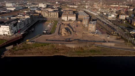Aerial-reveal-showing-a-construction-site-of-new-luxury-apartment-building-project-in-Noorderhaven-neighbourhood-in-Hanseatic-city-Zutphen,-The-Netherlands,-between-recreational-port-and-train-tracks