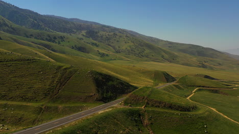 A-lone-car-drives-down-a-road-in-the-green-foothills-of-the-Tehachapi-mountains-in-Southern-California---aerial-view