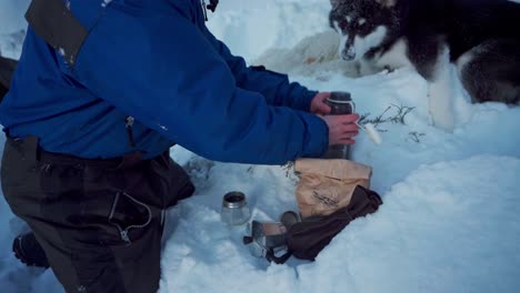 Guy-Making-Beverage-Using-An-Aluminum-Coffee-Maker-Next-To-Alaskan-Malamute-On-Snow-Landscape