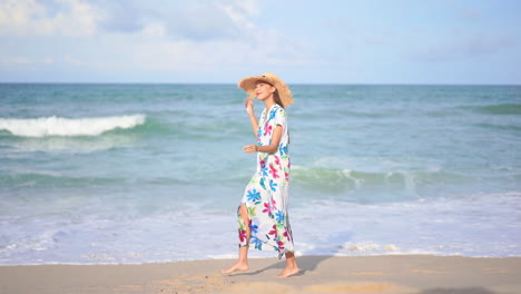 Zeitlupe-Einer-Asiatischen-Dame,-Die-In-Einem-Langen-Sommerkleid-Am-Strand-In-Thailand-Spazieren-Geht.-Sie-Hält-Ihren-Strohhut,-Weil-Es-Windig-Ist,-Zeitlupe-Nach-Seitenansicht