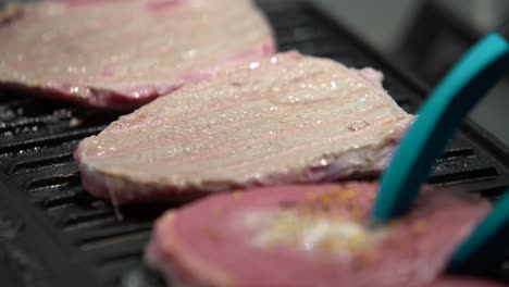 Flipping-Raw-Seasoned-Steaks-On-A-Iron-Griddle-With-Plastic-Tongs,-Static-Shot