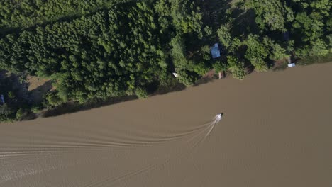 Aerial-top-down-shot-of-boat-cruising-on-brown-colored-amazon-river-and-arriving-dock-in-forest