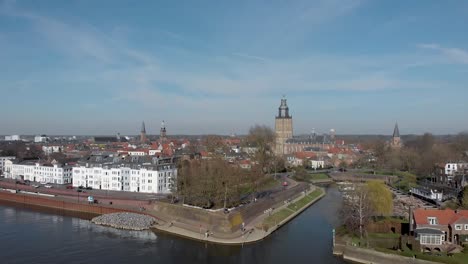 Aerial-approach-of-medieval-Hanseatic-city-Zutphen,-The-Netherlands,-with-entrance-to-small-Vispoorthaven-or-Gelre-port-connected-to-the-river-IJssel-against-a-bright-blue-sky-with-clouds