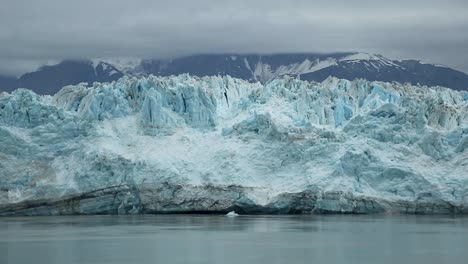 Panning-shot-of-huge-Hubbard-Glacier-in-Alaska,-USA-on-a-dark-cold-gloomy-overcast-cloudy-day-with-huge-snow-capped-mountains-in-the-background