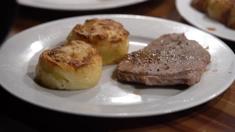 Grilled-steak-dish-with-potatoes-cakes-being-added-to-the-dish
