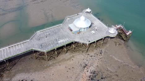 Bangor-seaside-pier-North-Wales-silver-spire-pavilion-low-tide-aerial-view-top-down-orbiting-right