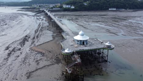 Bangor-seaside-pier-North-Wales-silver-spire-pavilion-low-tide-aerial-view-slow-push-in