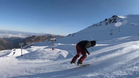 Snowboarder-riding-off-jump-in-the-snow-park-doing-a-360-indie-grab-on-a-bright-sunny-day-in-New-Zealand