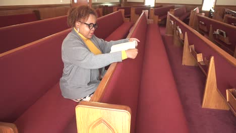 Mujer-Negra-Con-Anteojos-Leyendo-Felizmente-La-Palabra-De-Dios-En-Una-Iglesia-Vacía-En-Un-Día-Soleado