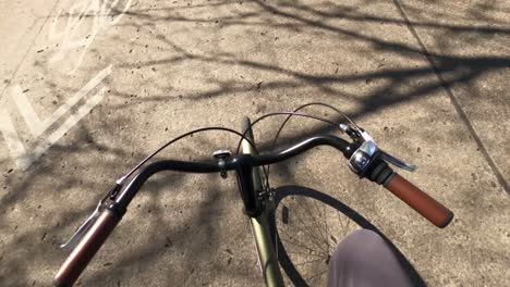 First-person-point-of-view-of-man-riding-green-bicycle-with-shadows-on-street