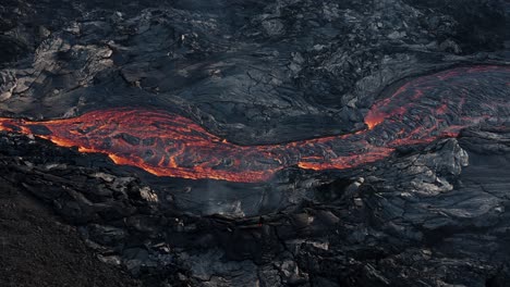 Lava-river-flows-on-earths-surface-surrounded-by-dark-basalt-rock