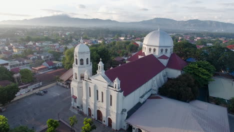 Eine-Leuchtend-Glänzende-Majestätische-Landschaftsdrohnenansicht-Einer-Basilikakirche-Der-Stadt-Mit-Fluss-Und-Bergen,-Batangas,-Philippinen