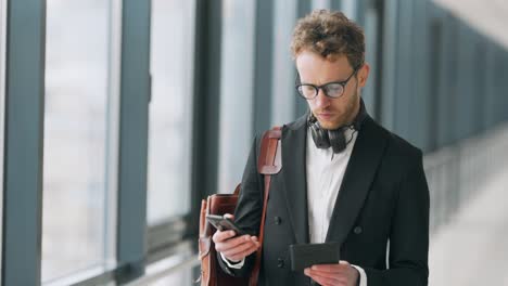 Stylish-man-with-tablet-and-phone-standing-in-the-hallway