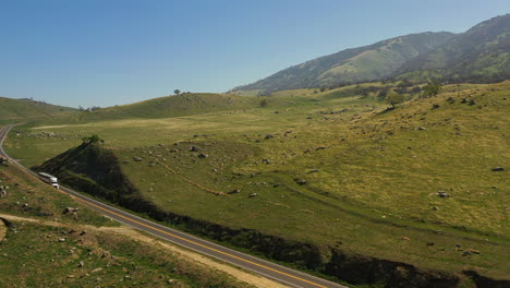 In-Spring-while-the-grass-is-green,-a-truck-drives-along-a-highway-in-Southern-California---aerial-view