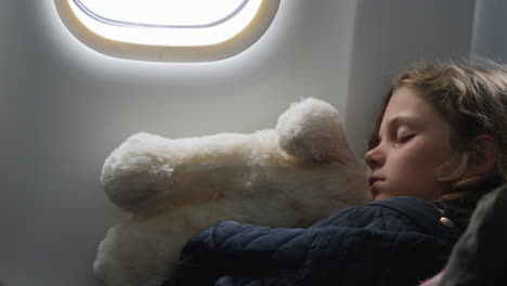 Young-girl-snuggles-with-stuffed-animal-while-sleeping-during-airplane-flight