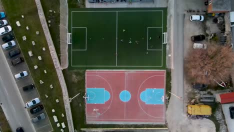 Drone-flight-from-bird's-eye-view-over-a-small-soccer-field-next-to-an-basketball-field-where-a-game-is-being-played