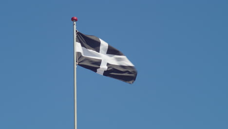 Cornwall-Flag---Saint-Piran's-Flag-On-Pole-Waving-In-The-Wind-With-Blue-Sky-In-The-Background