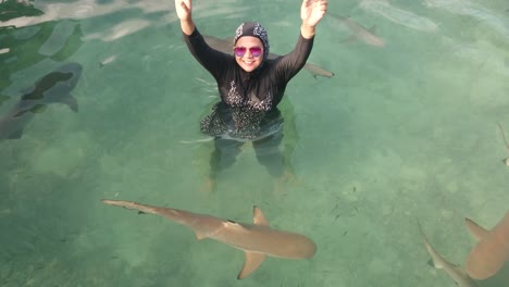 A-female-tourist-wearing-glasses-having-fun-with-baby-sharks-swimming-around-her