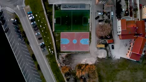 High-Drone-flight-from-bird's-eye-view-over-a-small-soccer-field-next-to-an-basketball-field-where-a-game-is-being-played-near-a-street-with-cars