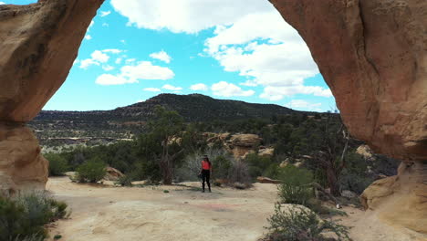 Luftaufnahme-Einer-Jungen-Fotografin,-Die-Unter-Einem-Erstaunlichen-Natürlichen-Bogen-In-Der-Wüstenlandschaft-Von-New-Mexico-Steht,-Navajo-nationalgebiet,-Drohnenaufnahme