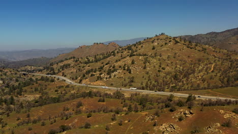 Steady-traffic-flows-along-a-highway-through-the-Tehachapi-Mountains-on-a-bright-but-hazy-day---aerial-view