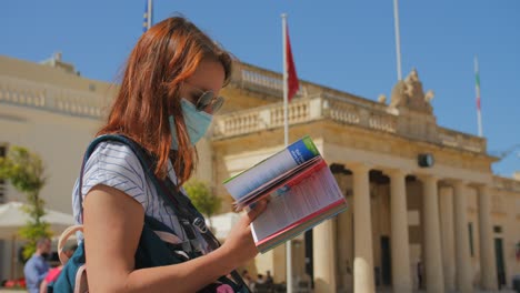 Young-female-traveler-on-vacation-in-Valletta-Malta-outside-the-Grandmasters-Palace-checking-her-guide-book-for-references