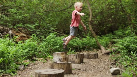 Active-little-blonde-child-boy-playing-jumping-from-wooden-logs