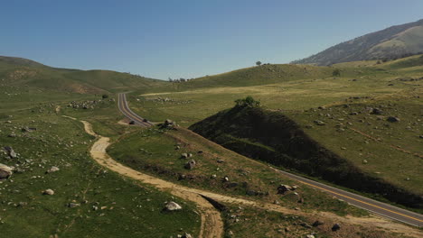A-lone-car-speeds-along-a-road-in-the-Tehachapi-Mountains-in-spring-with-fresh-new-spring-grass---aerial-view