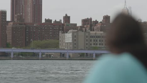 Rack-Fokusaufnahme-Einer-Frau,-Die-Es-Genießt,-Draußen-Zu-Sein,-Während-Sie-Auf-Den-East-River-Gegenüber-Von-Lower-Manhattan-Blickt