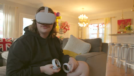 Teenager-Zu-Hause,-Der-Ein-Virtual-Reality-Headset-Trägt-Und-Controller-In-Der-Hand-Hält,-Blickt-In-Eine-Simulierte-Welt