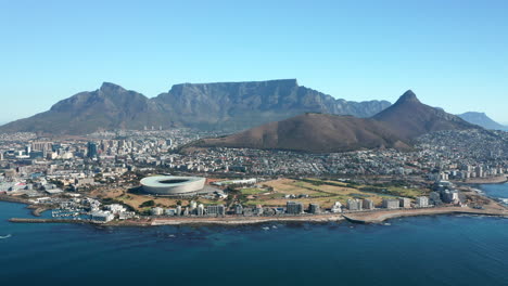 Cape-Town-Stadium-At-The-Sea-Coast-In-Cape-Town,-South-Africa-With-Signal-Hill-And-Table-Mountain-National-Park-In-Background