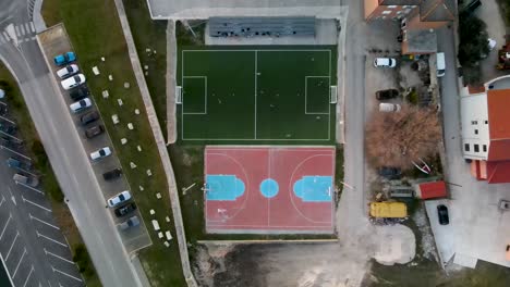 High-Drone-flight-from-bird's-eye-view-over-a-small-soccer-field-next-to-an-basketball-field-where-a-game-is-being-played