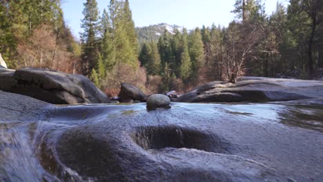 River-Trickles-Around-a-Granite-Stone-With-Mountain-Pine-Forest-In-Background