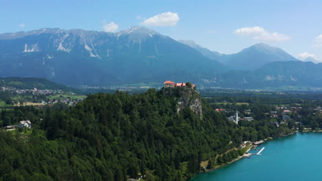 Bled-Castle-Museum-On-A-Precipice-With-Dense-Foliage-Overlooking-Lake-Bled-In-Slovenia-With-Beautiful-Mountain-Range-In-Background