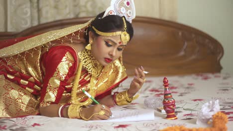 Indian-bengali-bride-smoking-cigarette-and-writing-in-notebook-with-pen-and-paper-at-home,-gold-jewellery
