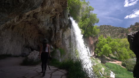 Mujer-Joven-Caminando-En-Una-Cueva-Bajo-Majestuosas-Cascadas