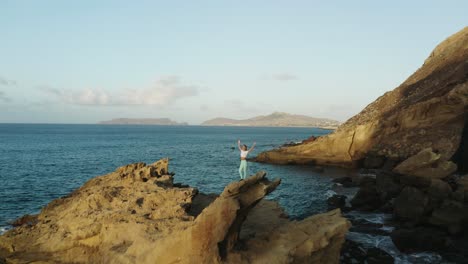 Adventure-woman-with-arms-up-stands-on-jagged-rock-on-coast-of-Porto-Santo