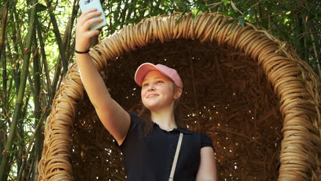 Young-girl-taking-selfie-in-wicker-egg-shaped-seat-in-oriental-bamboo-forest-close-up