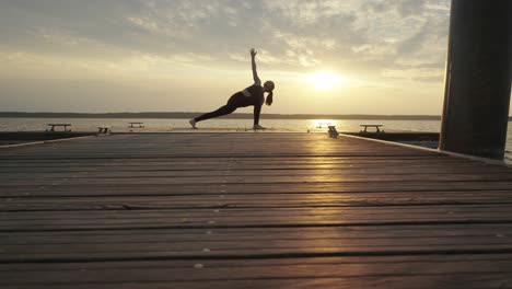 Young-woman-doing-yoga-stretches-on-pier-at-sunset,-overlooking-calm-sea