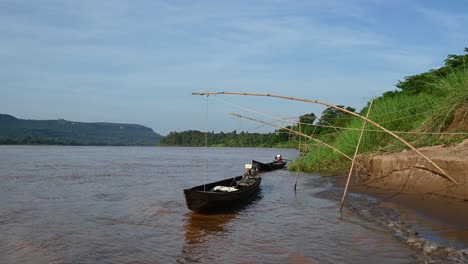 Long-boats-moored-at-the-edge-of-the-Mekong-river-with-gentle-waves-lapping-the-shore