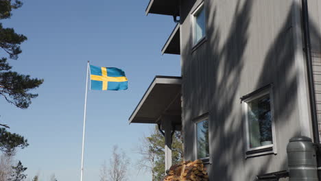 Schwedische-Flagge-Am-Fahnenmast-Weht-Bei-Starkem-Wind-In-Zeitlupe-Neben-Der-Villa