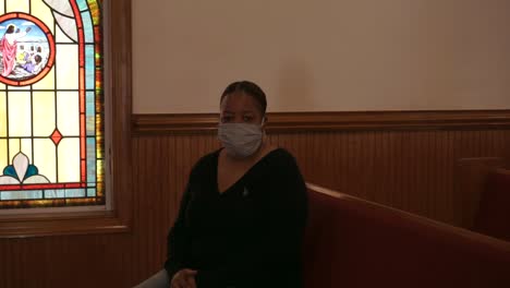 Schwarze-Afroamerikanerin,-Die-Während-Einer-Pandemie-In-Einer-Leeren-Kirche-Sitzt-Und-Eine-Maske-Trägt,-Die-Direkt-In-Die-Kamera-Schaut