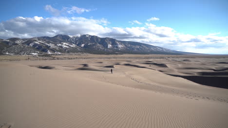 One-Lonely-Person-Walking-on-Dune-With-Snow-Capped-Mountain-Hills-in-Background