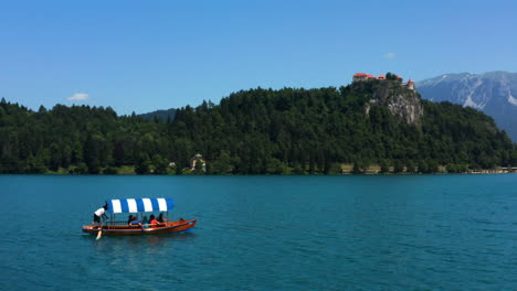 Touristen,-Die-Auf-Einem-Pletna-boot-Auf-Dem-Bledsee-Mit-Blick-Auf-Die-Wallfahrtskirche-Und-Die-Bergburg-In-Slowenien-Fahren