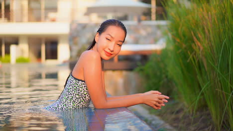 Close-up-of-a-pretty-young-woman-leaning-along-the-edge-of-a-resort-swimming-pool