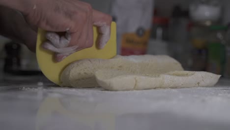 Close-up-of-chef-cutting-fresh-dough-in-pieces-in-kitchen-bakery