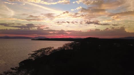 A-magical-sunset-near-a-lake-in-Costa-Rica,-shot-with-a-drone-flying-over-the-coastline-and-the-forest