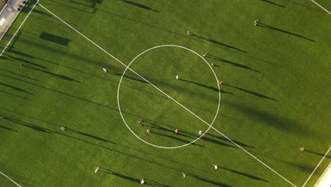 Aerial-top-down-view-of-a-green-soccer-field-with-people-playing